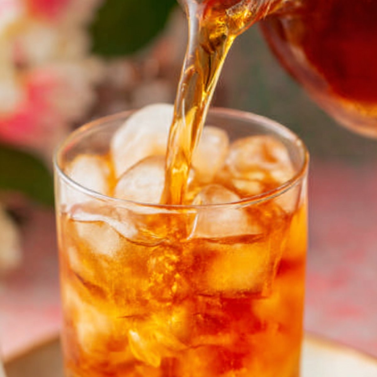 A close-up image of iced tea being poured over a glass filled with ice cubes.