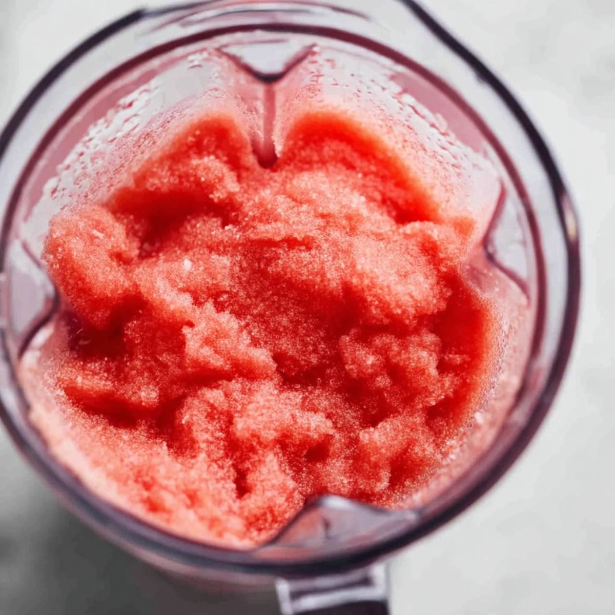 A close-up of blended watermelon slushie in a blender, with a smooth and icy texture, ready to be served.