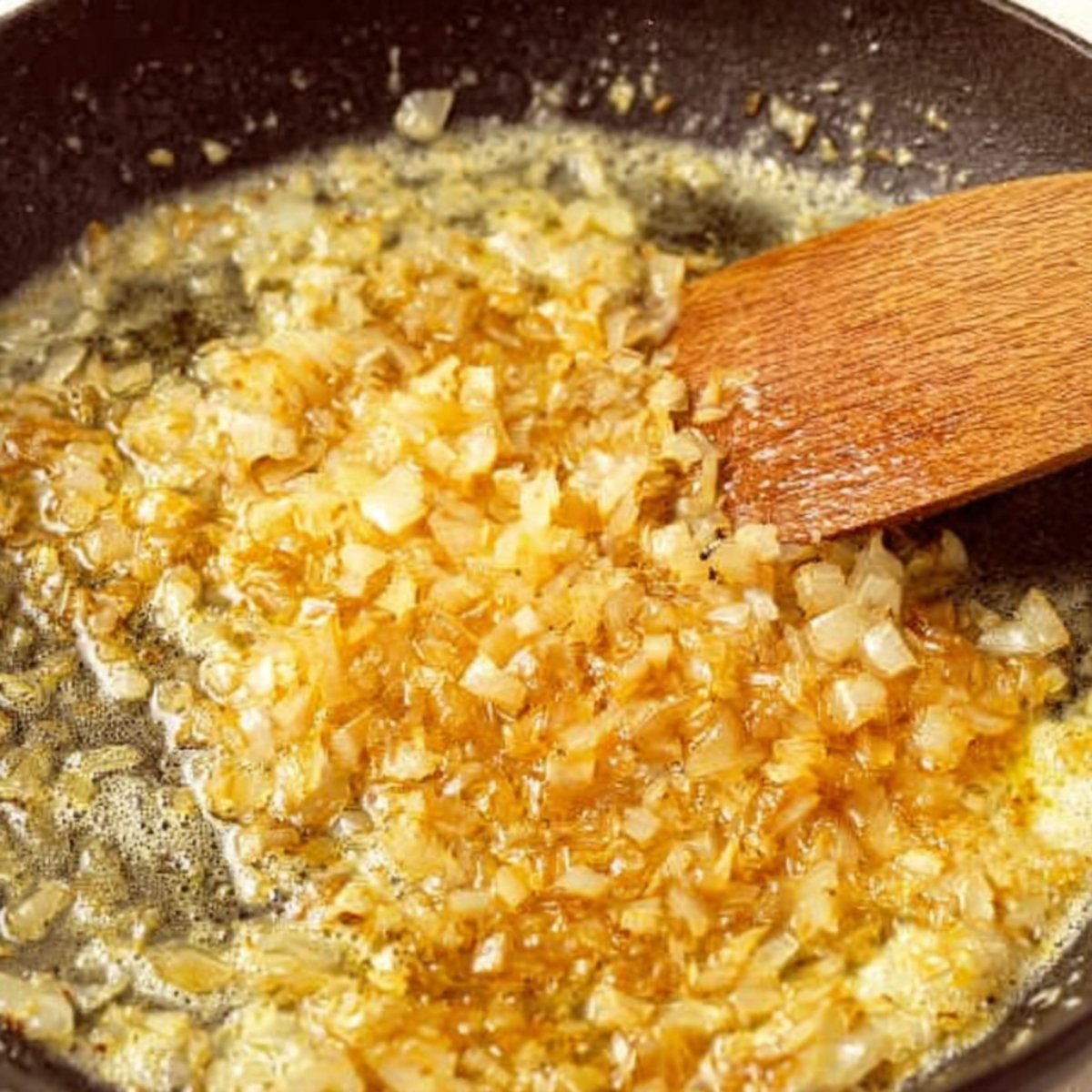 Cooking diced onions in butter until golden brown in a pan, with a wooden spoon stirring them.