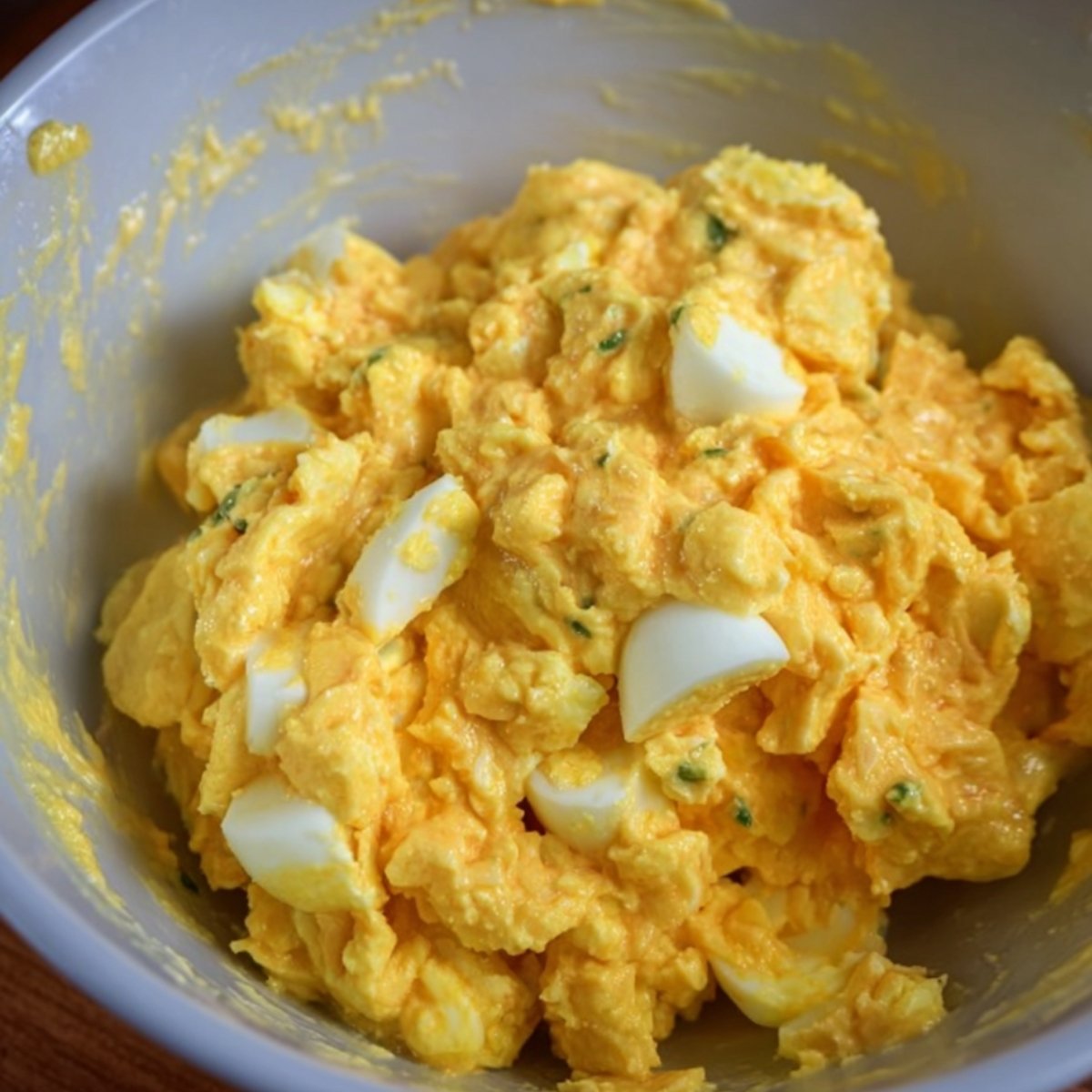 A bowl of creamy egg salad, with chunks of boiled eggs mixed in.