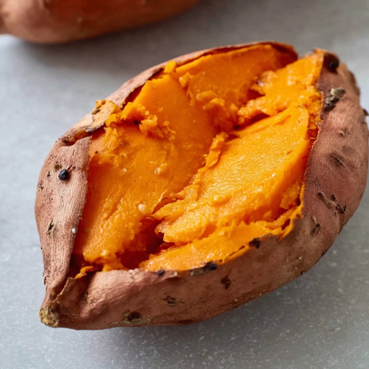 Close up of a roasted sweet potato, split open to reveal its vibrant orange flesh. The soft, caramelized interior contrasts with the crispy skin, highlighting the natural sweetness of the sweet potato.