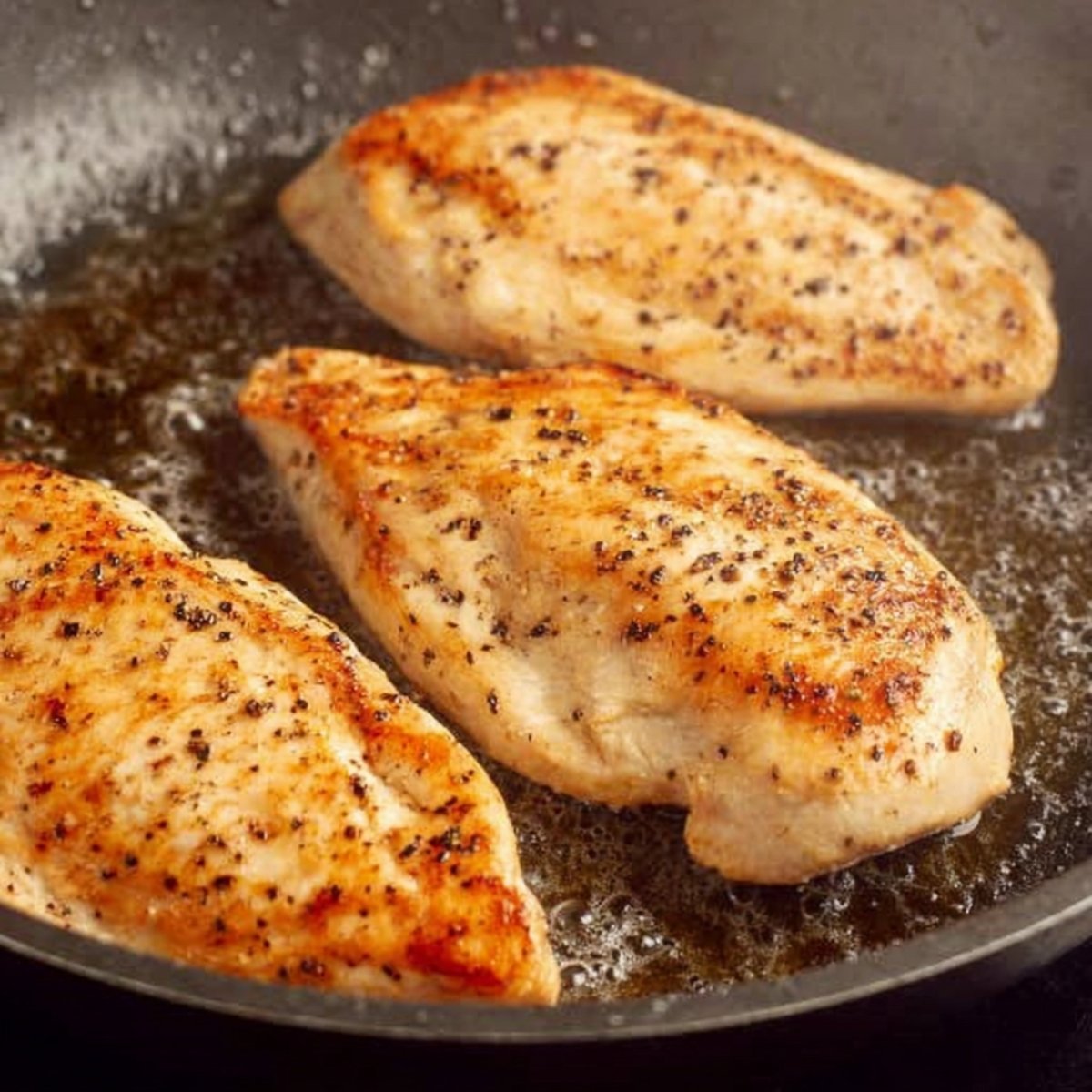 Searing seasoned chicken breasts in a pan with a golden-brown crust.