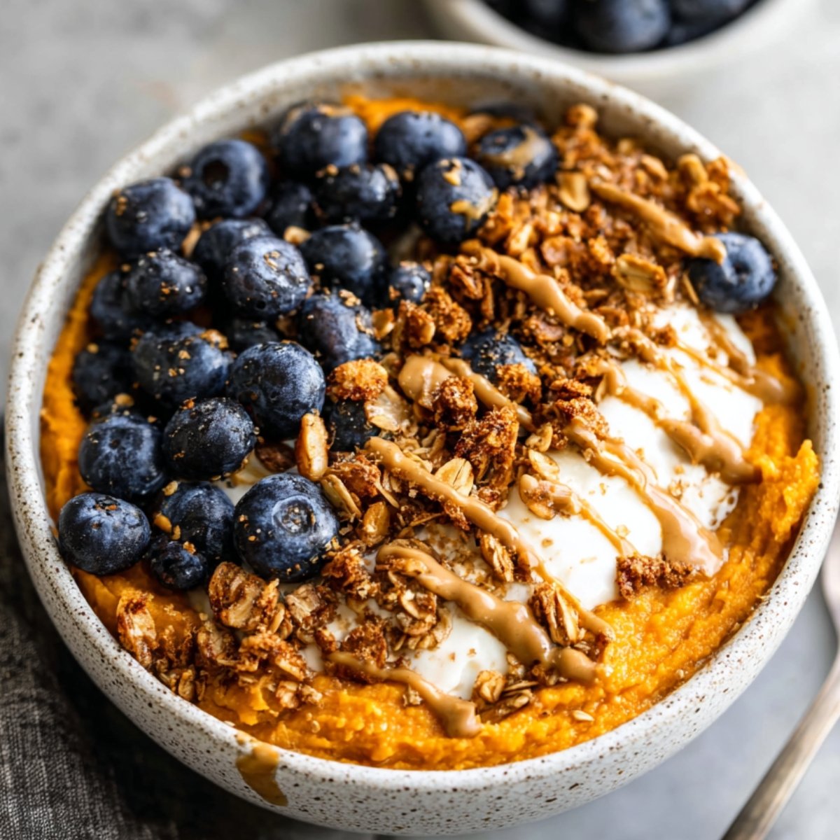 A delicious Sweet Potato Breakfast Bowl topped with fresh blueberries, granola, and a drizzle of nut butter. The smooth, orange mashed sweet potato is paired with creamy yogurt, offering a healthy and satisfying breakfast.