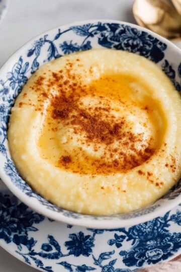 A bowl of Rømmegrøt, smooth porridge garnished with a drizzle of butter and a sprinkle of cinnamon. The bowl is placed on a floral-patterned plate.
