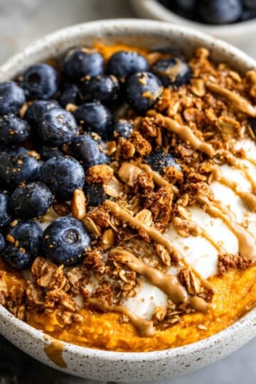 A delicious Sweet Potato Breakfast Bowl topped with fresh blueberries, granola, and a drizzle of nut butter. The smooth, orange mashed sweet potato is paired with creamy yogurt, offering a healthy and satisfying breakfast.